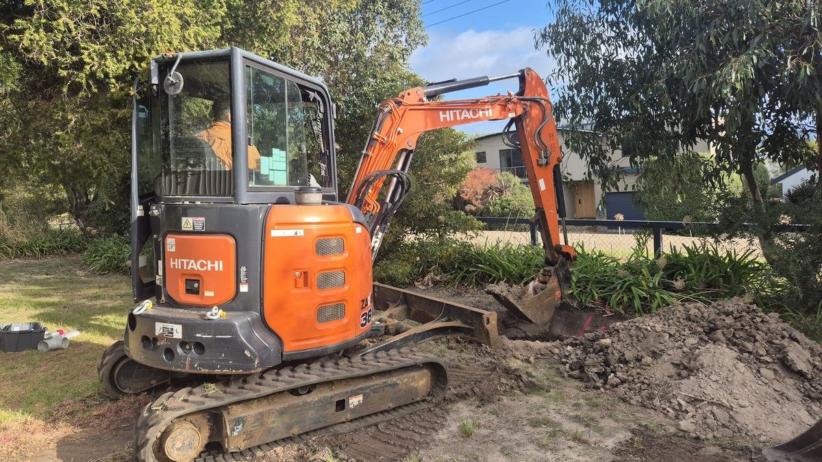 Mini excavator digging a trench for sewer renewal at a coastal home